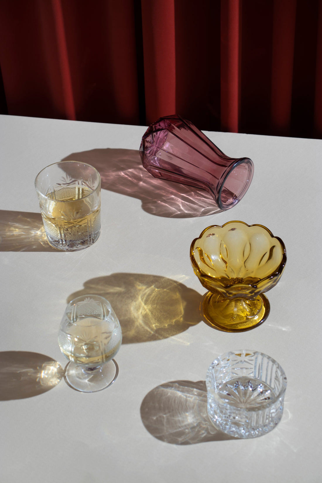 Copas de cristal tallado con destilados sobre mesa iluminada, reflejando una estética elegante y curada.